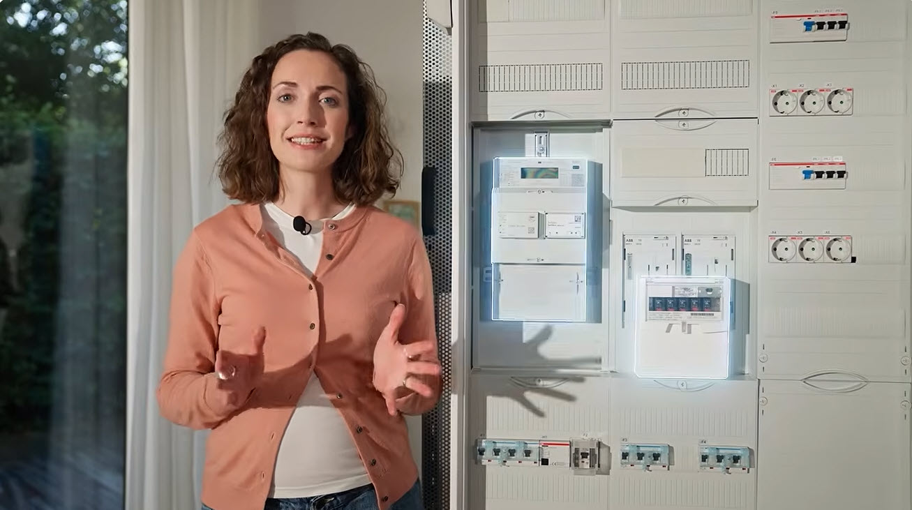 Frau steht neben einem Hausanschlusskasten und hält ihre Hände offen.