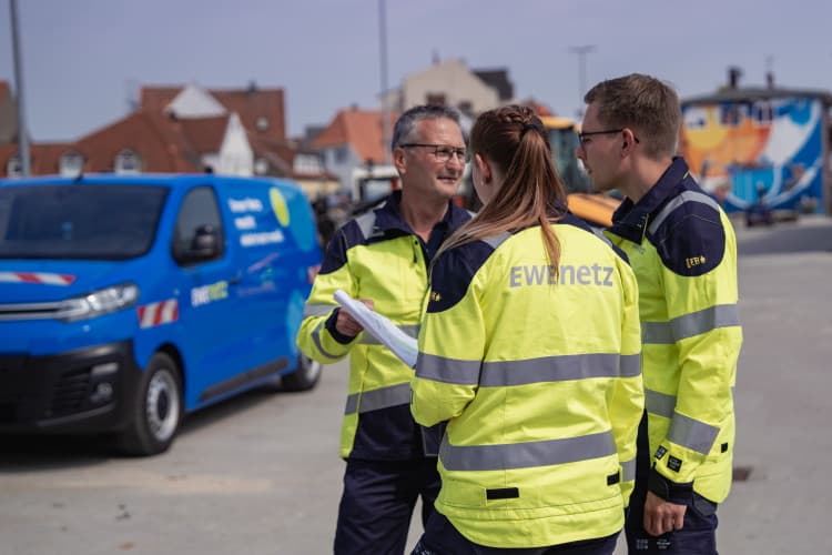 Drei EWE-NETZ-Mitarbeitende in Warnkleidung besprechen Unterlagen auf einer Baustelle.