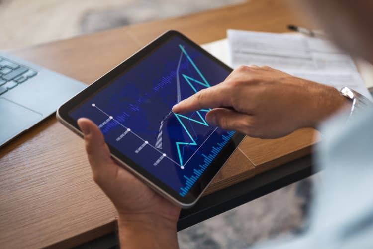 Eine Hand wischt über ein Tablet, auf dem eine Leistungskurve zu sehen ist