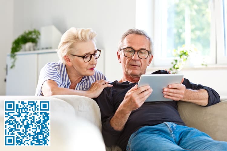 Ein älteres Ehepaar schaut auf ein Tablet, unten links ist ein QR-Code zu sehen