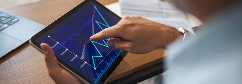Eine Hand wischt über ein Tablet, auf dem eine Leistungskurve zu sehen ist